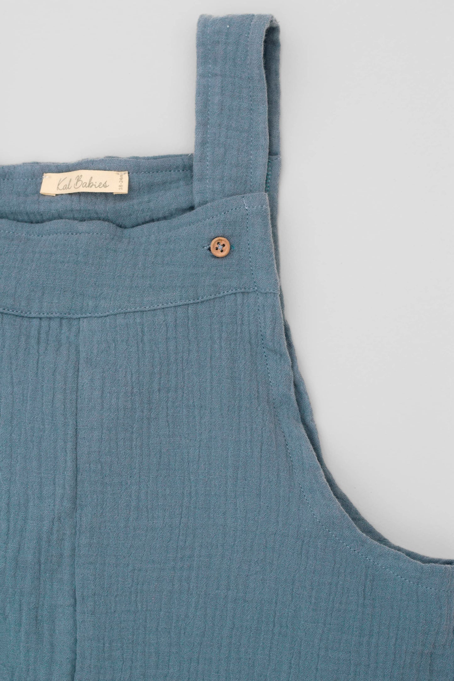 Organic cotton short leg overall in blue muslin. Loose fit and buttoned straps and cargo pockets. Front detail