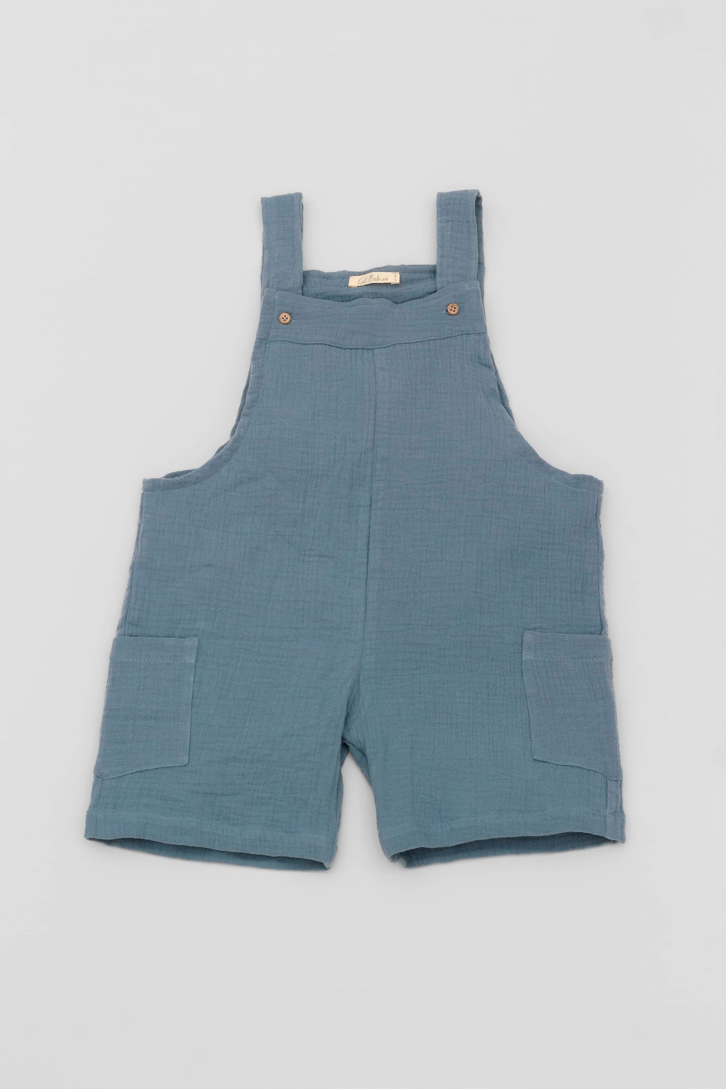 Organic cotton short leg overall in blue muslin. Loose fit and buttoned straps and cargo pockets. Front view