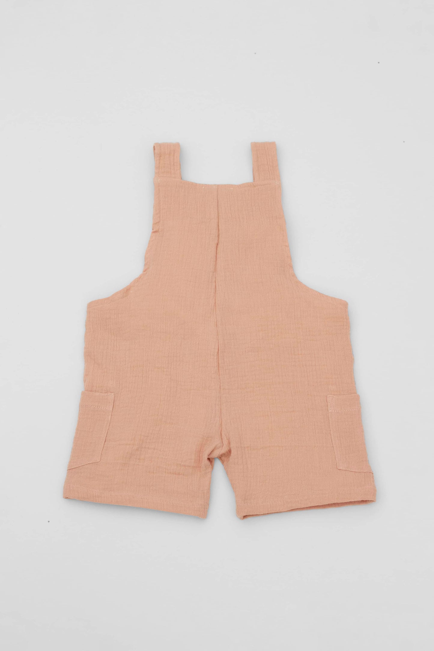 Organic cotton short leg overall in clay muslin. Loose fit and buttoned straps and cargo pockets. Backt view
