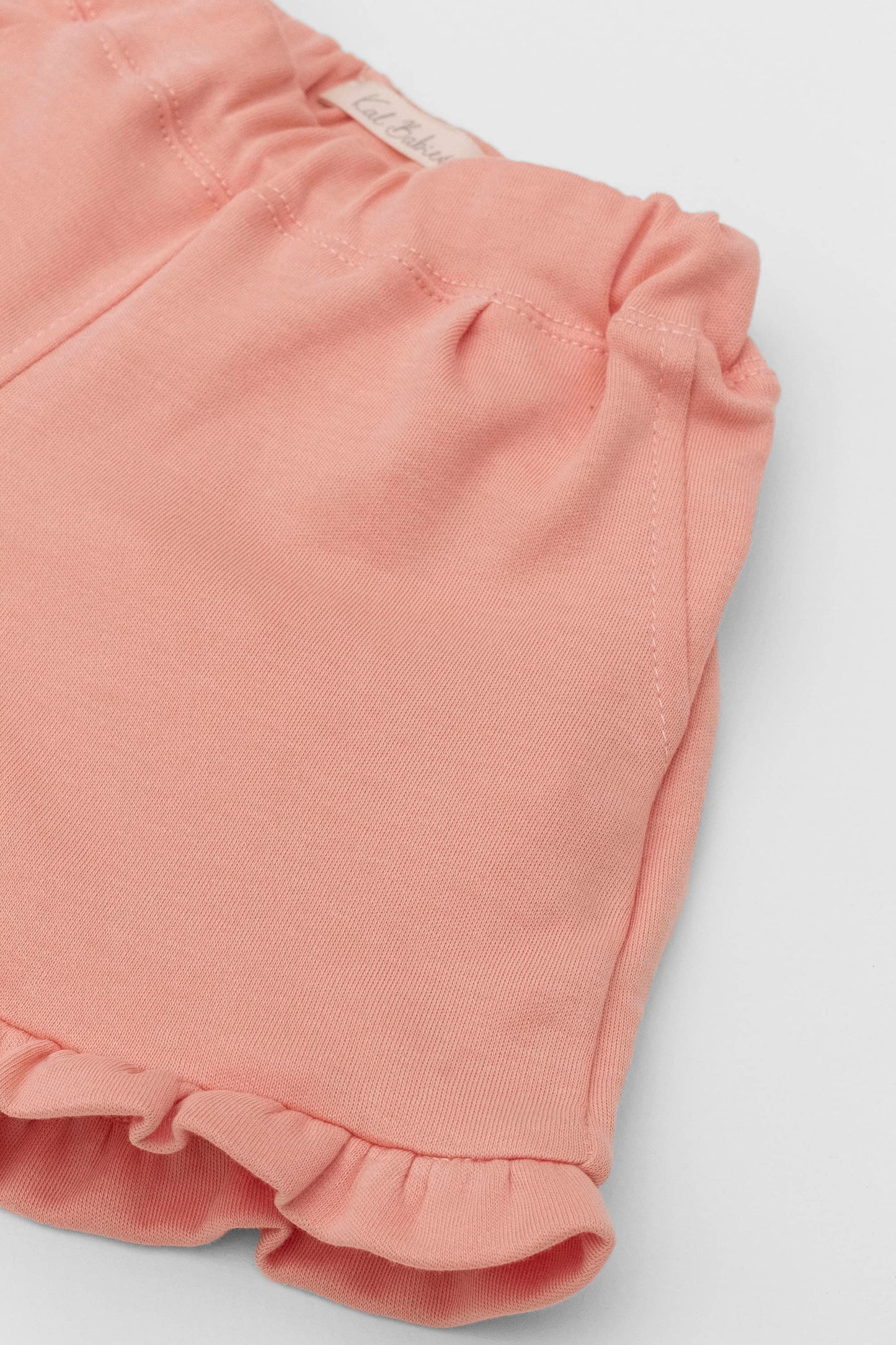 Organic pima cotton shorts with ruffle hem, elasticized waist and fake pockets. soft melon. Front detail