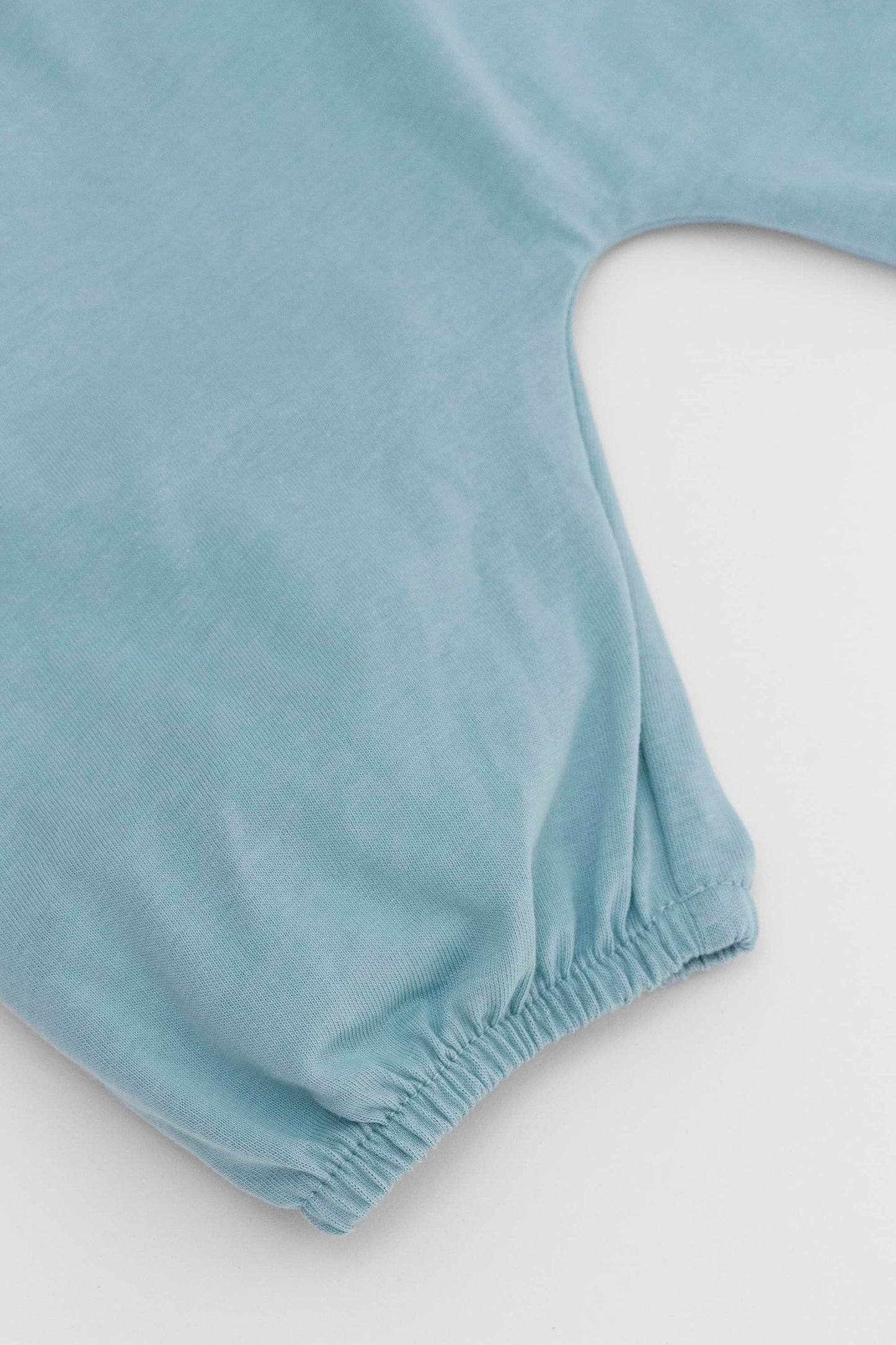 Smocked blue organic romper with straps and embroidery. Leg detail