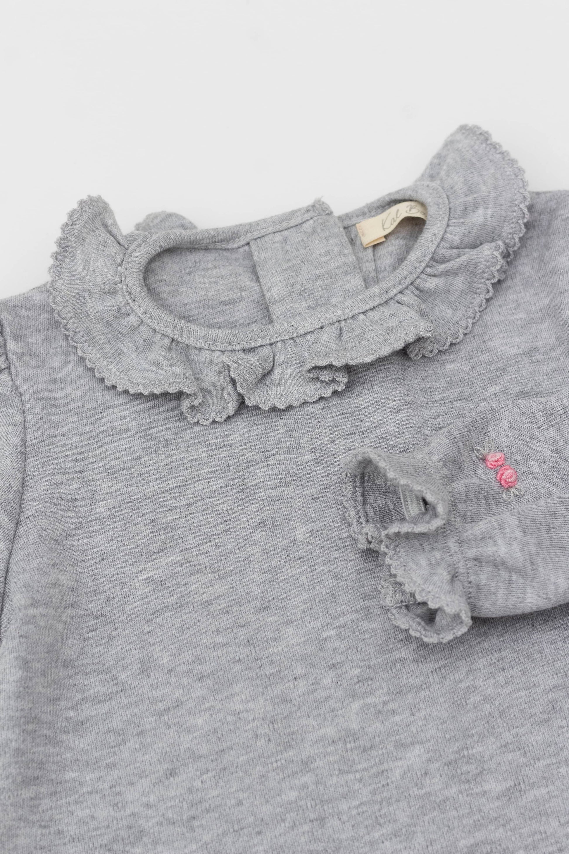 Bodysuit with ruffle collar and and long puff sleeves. Floral embroidery on sleeves. Snaps inseam. Back button closure. Heather grey color.  Embroidery detail