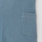 Organic cotton short leg overall in blue muslin. Loose fit and buttoned straps and cargo pockets. Pocket detail