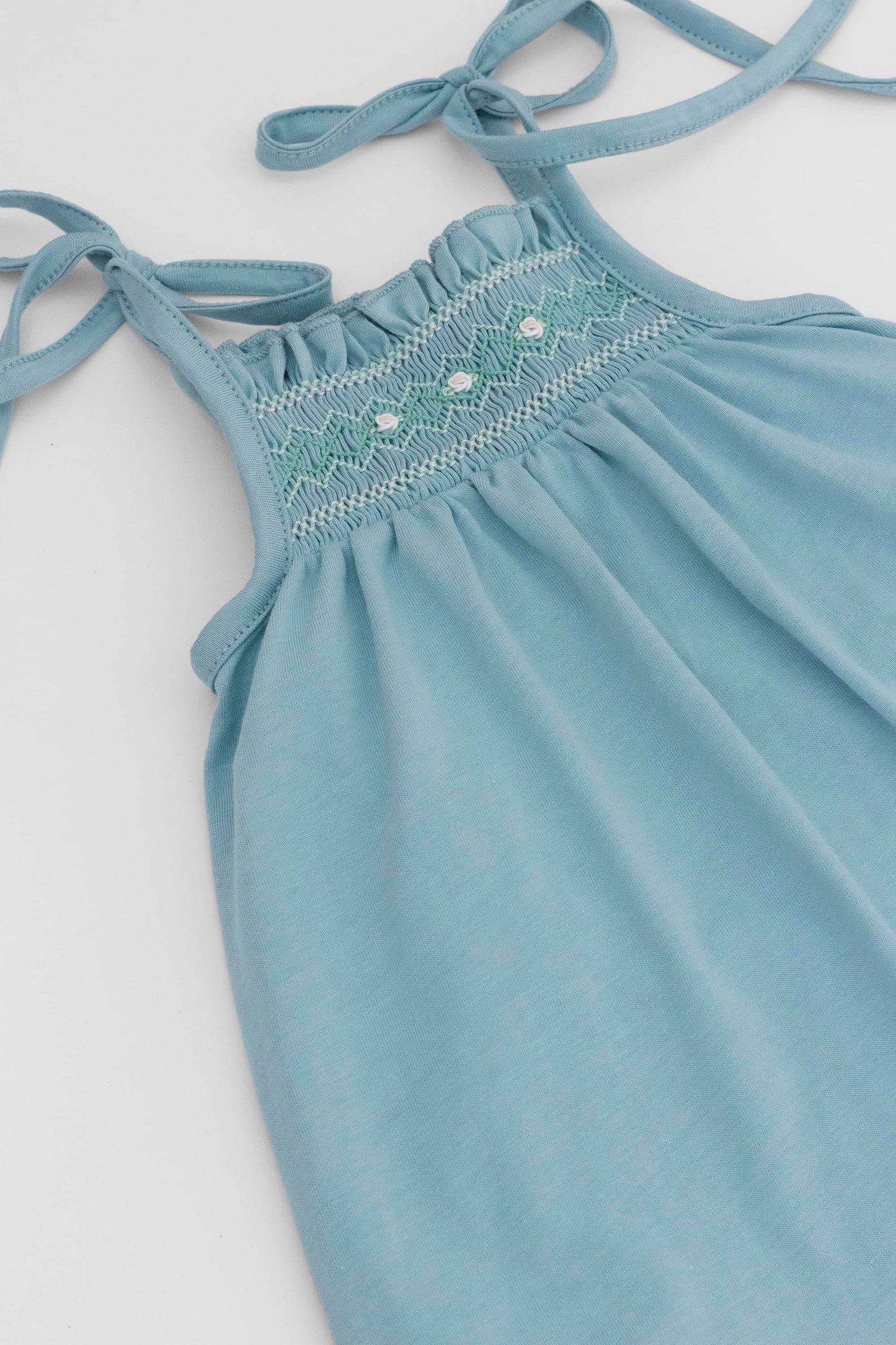 Smocked blue organic romper with straps and embroidery . Front detail view