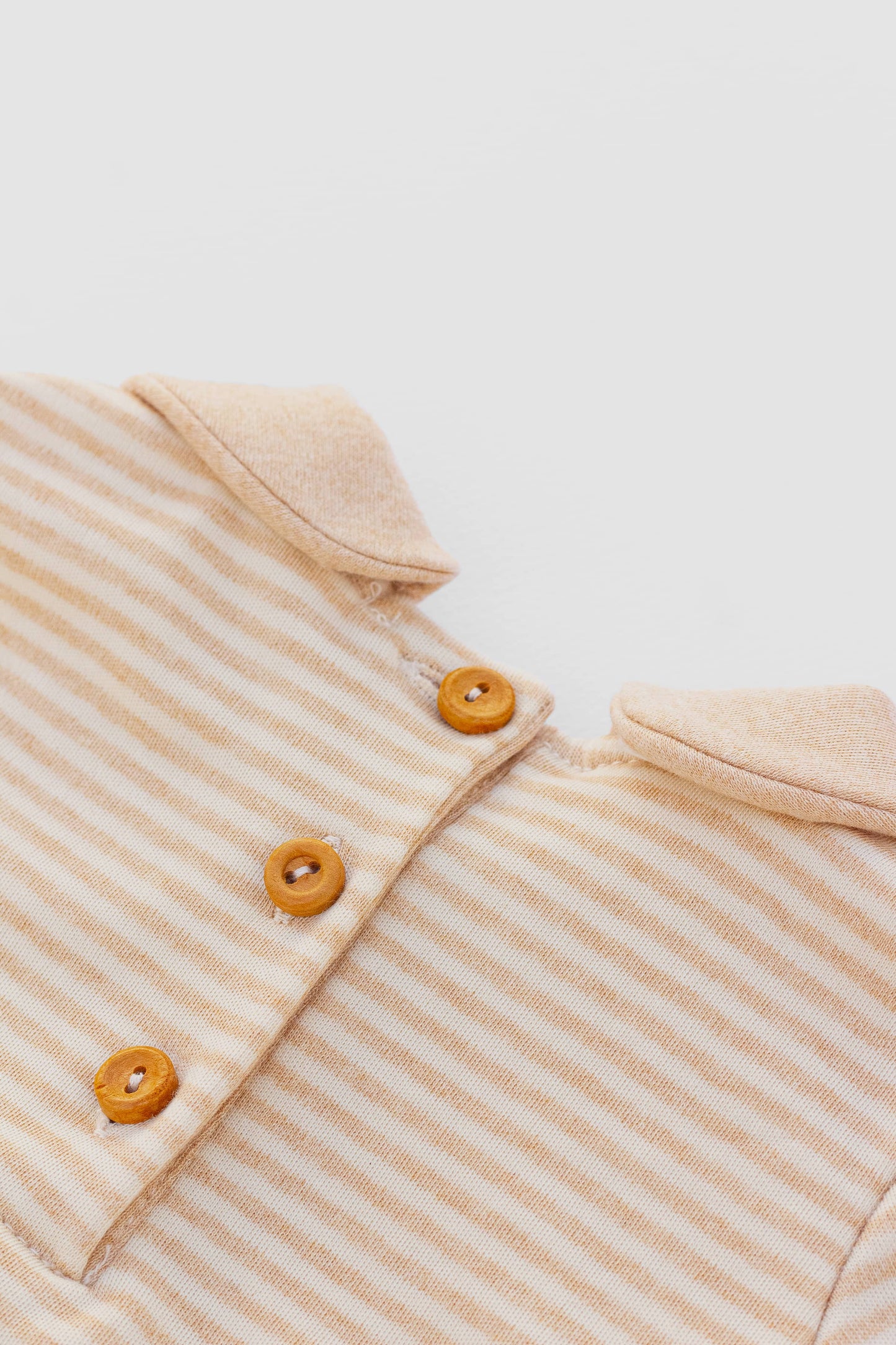 Contrasted collar bodysuit. Short-sleeve with button and strap. Back button closure. Contrasting piping and snaps inseam.  Sand stripes certified organic pima cotton. Back button closure detail